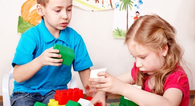 Two young children build with blocks together.